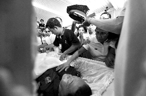 28日，兇手門多薩身著警服躺在棺木里。